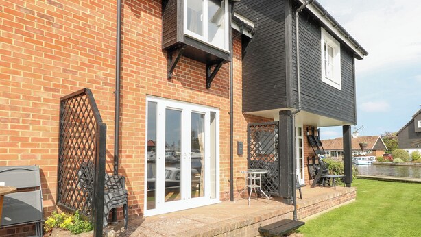 A two-story house with a brick facade, a balcony with outdoor seating, and a view of a canal.