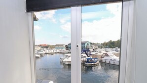 A view from a window overlooking a marina with boats docked, a clear sky, and buildings in the background.