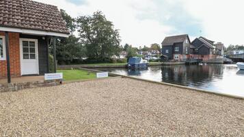 A riverside property with a gravel driveway, a boat dock, and a row of houses in the background.