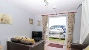 A living room with a sofa, a TV, and a view of boats through a glass door.