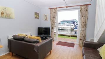 Ein Wohnzimmer mit einer Couch, einem Fernseher und Blick auf Boote durch eine Glastür.