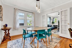 A dining area with a wooden table and teal chairs, a patterned rug, and a view of the outdoors through a window. - Pet Friendly Cute Cottage - Walk to PC/Downtown (Clinton)