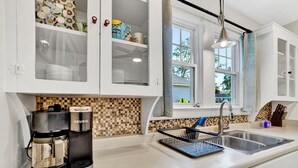 A modern kitchen with white cabinets, a coffee maker, a tiled backsplash, and a window with a view of the outside. - Pet Friendly Cute Cottage - Walk to PC/Downtown (Clinton)