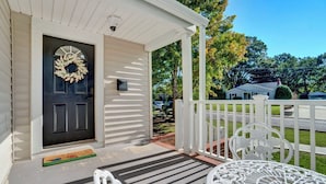 A porch with a black door, white railing, and a table with a decorative top. - Pet Friendly Cute Cottage - Walk to PC/Downtown (Clinton)