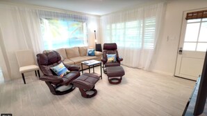 Una sala de estar con un sofá color beige, dos sillones de cuero marrón, una mesita de centro y un televisor.