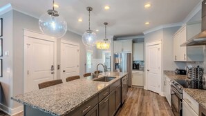 Una cocina moderna con encimeras de granito, electrodomésticos de acero inoxidable e iluminación colgante.