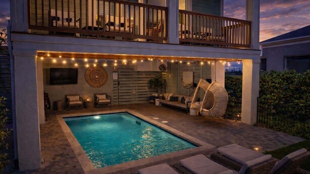 Una casa de dos pisos con piscina, mobiliario exterior e iluminación de luces colgantes.
