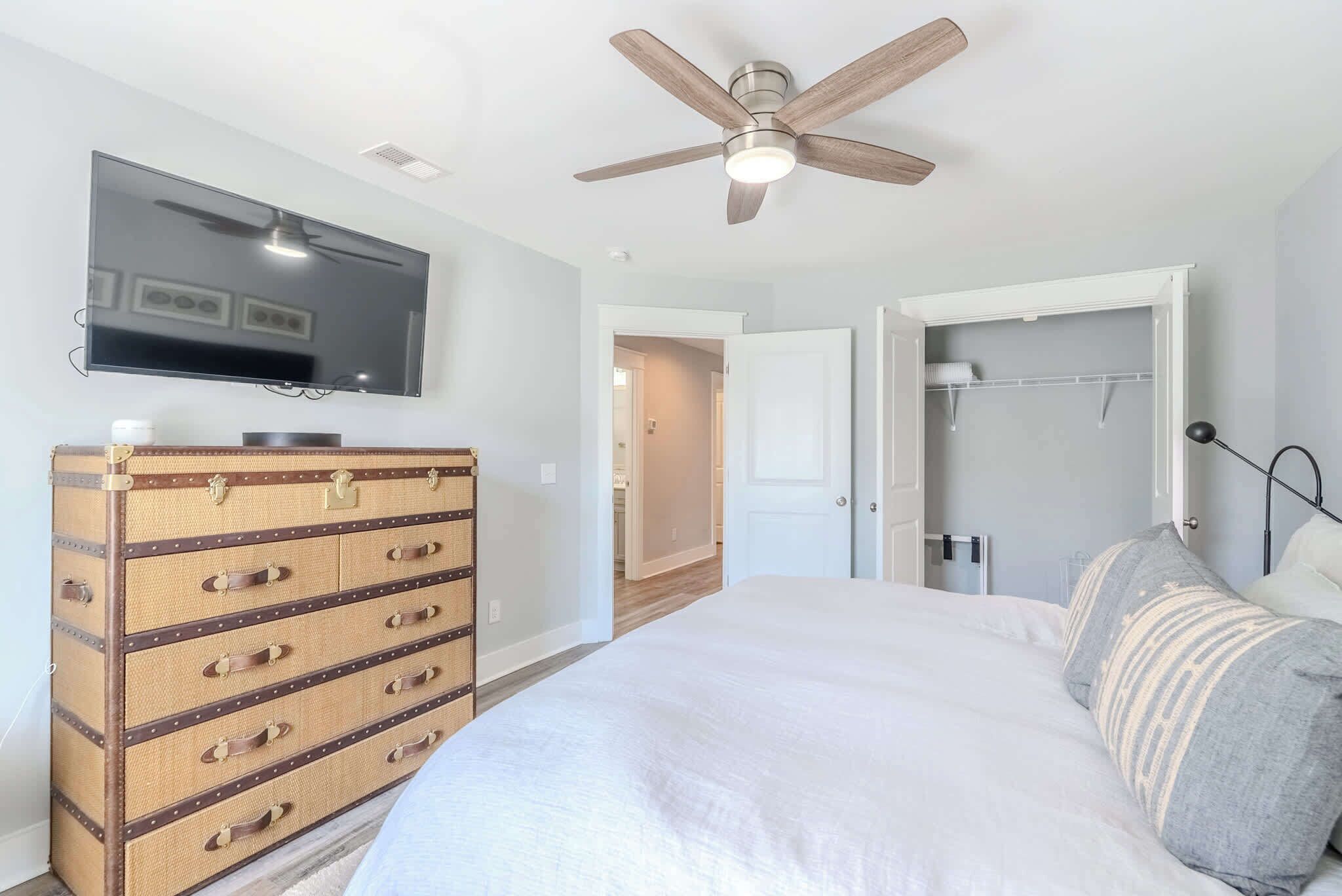 A bedroom with a bed, a dresser, a ceiling fan, and a television.