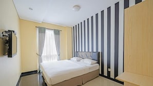 Una camera d'albergo con un letto, una televisione, una finestra con tende e un muro a righe.