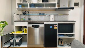 Eine kompakte Küche mit Geschirrspüler, Kühlschrank, Mikrowelle und verschiedenen Küchenutensilien in Regalen.