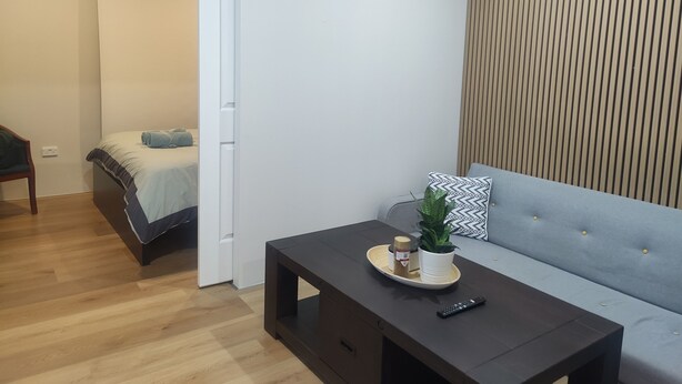 Ein modernes Zimmer mit einem Bett, einem Sofa, einem kleinen Tisch mit Pflanze und Tablett sowie Holzboden.