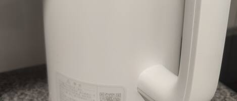 Una tetera eléctrica blanca con un código QR y un botón de encendido sobre una encimera de granito.