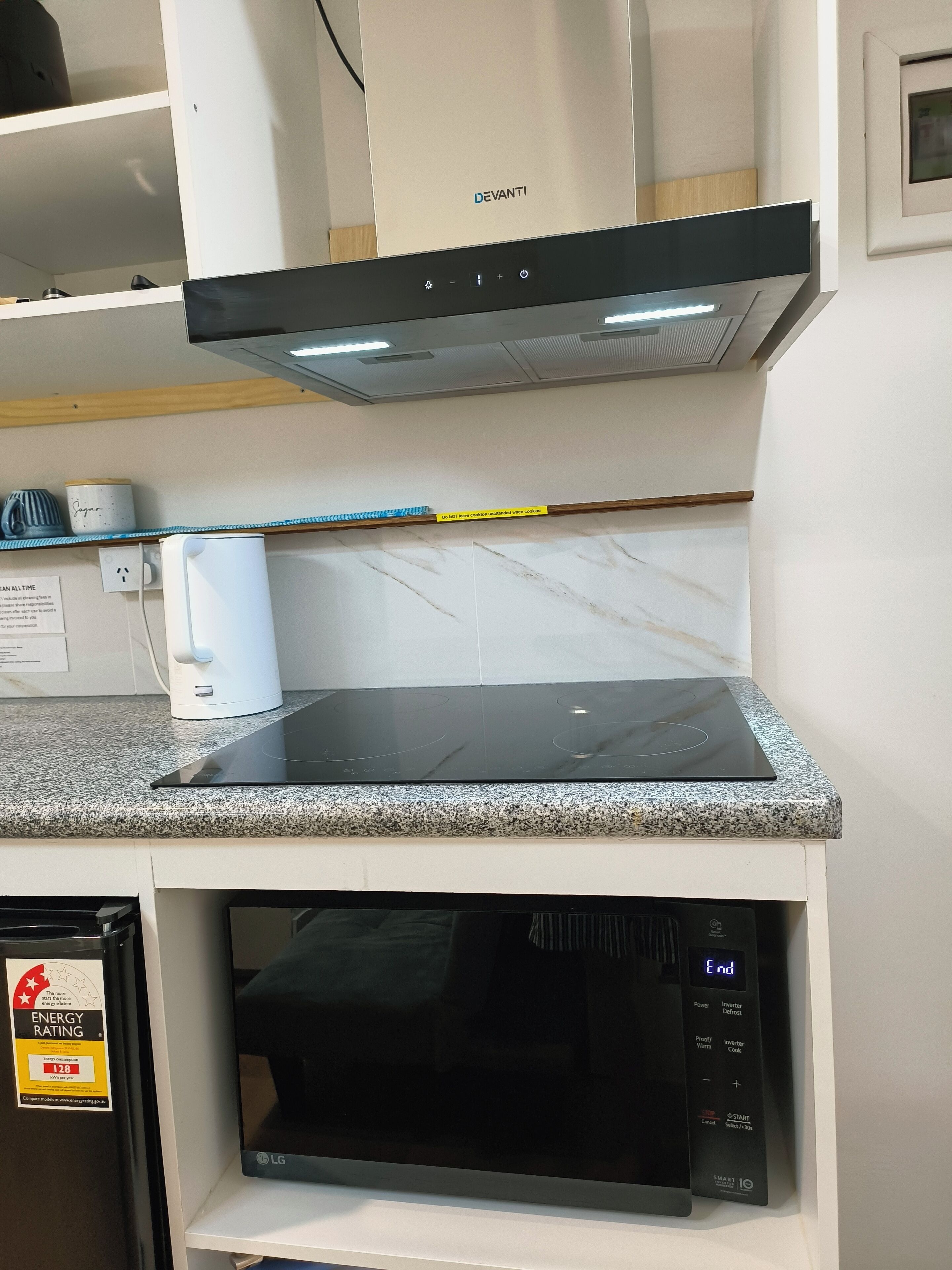 Eine Küche mit einer schwarzen Induktionskochplatte, einer Mikrowelle und einem weißen Backofen.