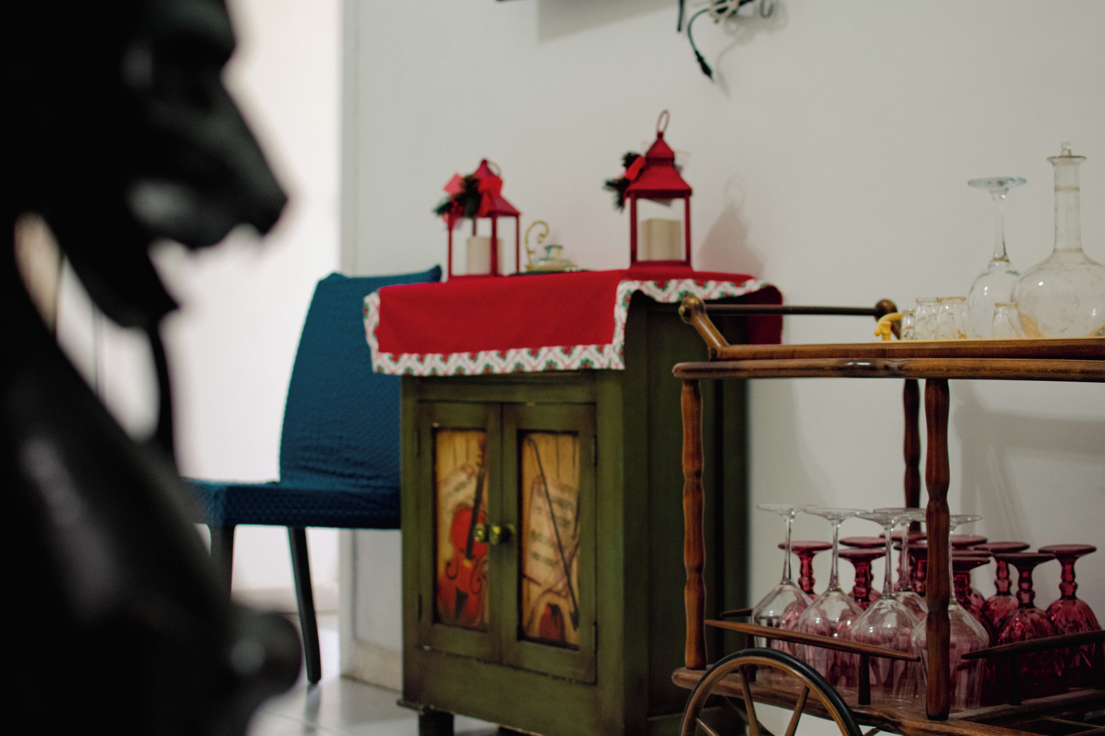 Une pièce comprenant un chariot d’époque servant à présenter des verres à vin et un petit meuble recouvert d’un tissu à motifs rouges et blancs.
