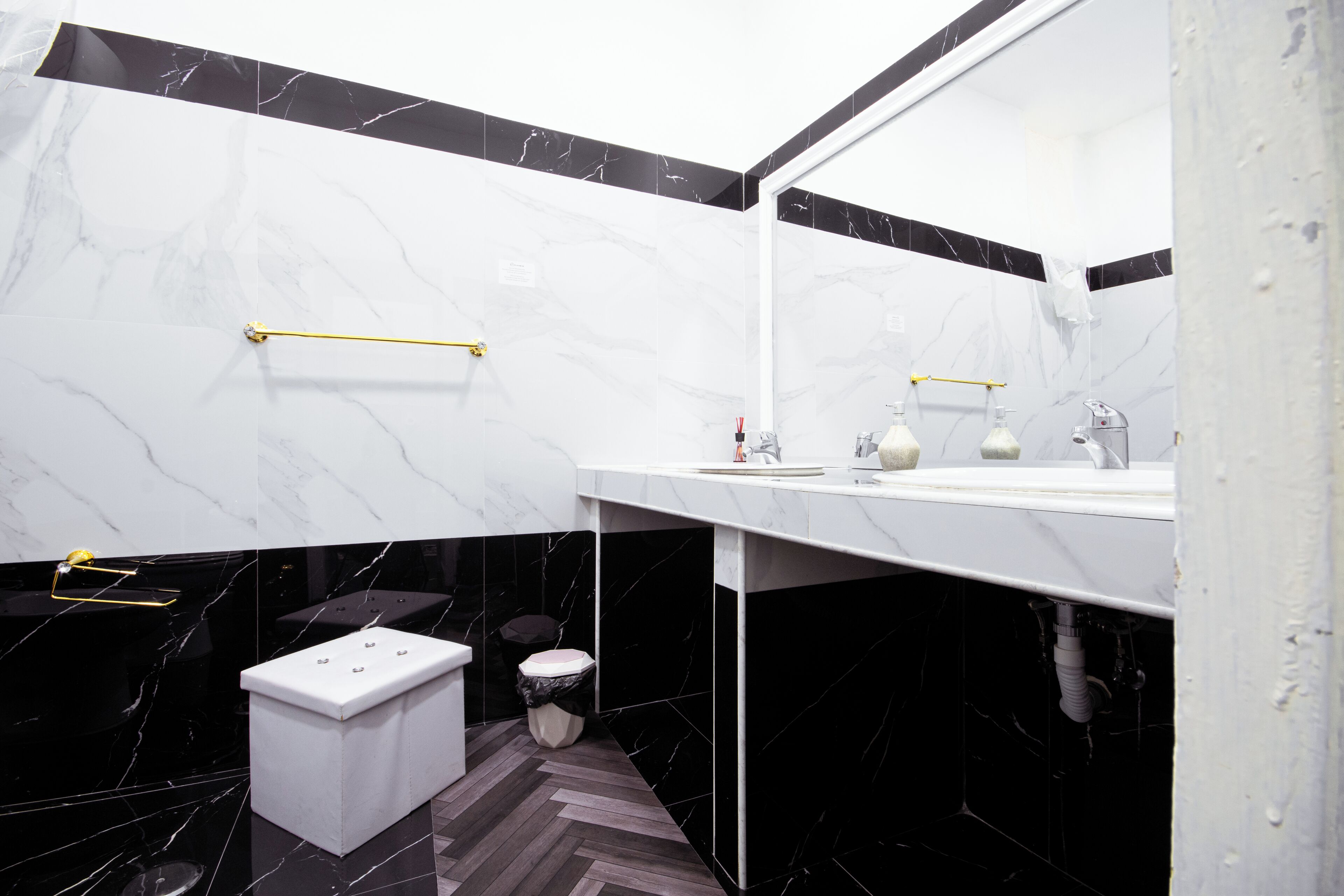 Een moderne badkamer met een wit marmeren wastafelmeubel, zwarte marmeren wanden en een visgraatvloer.