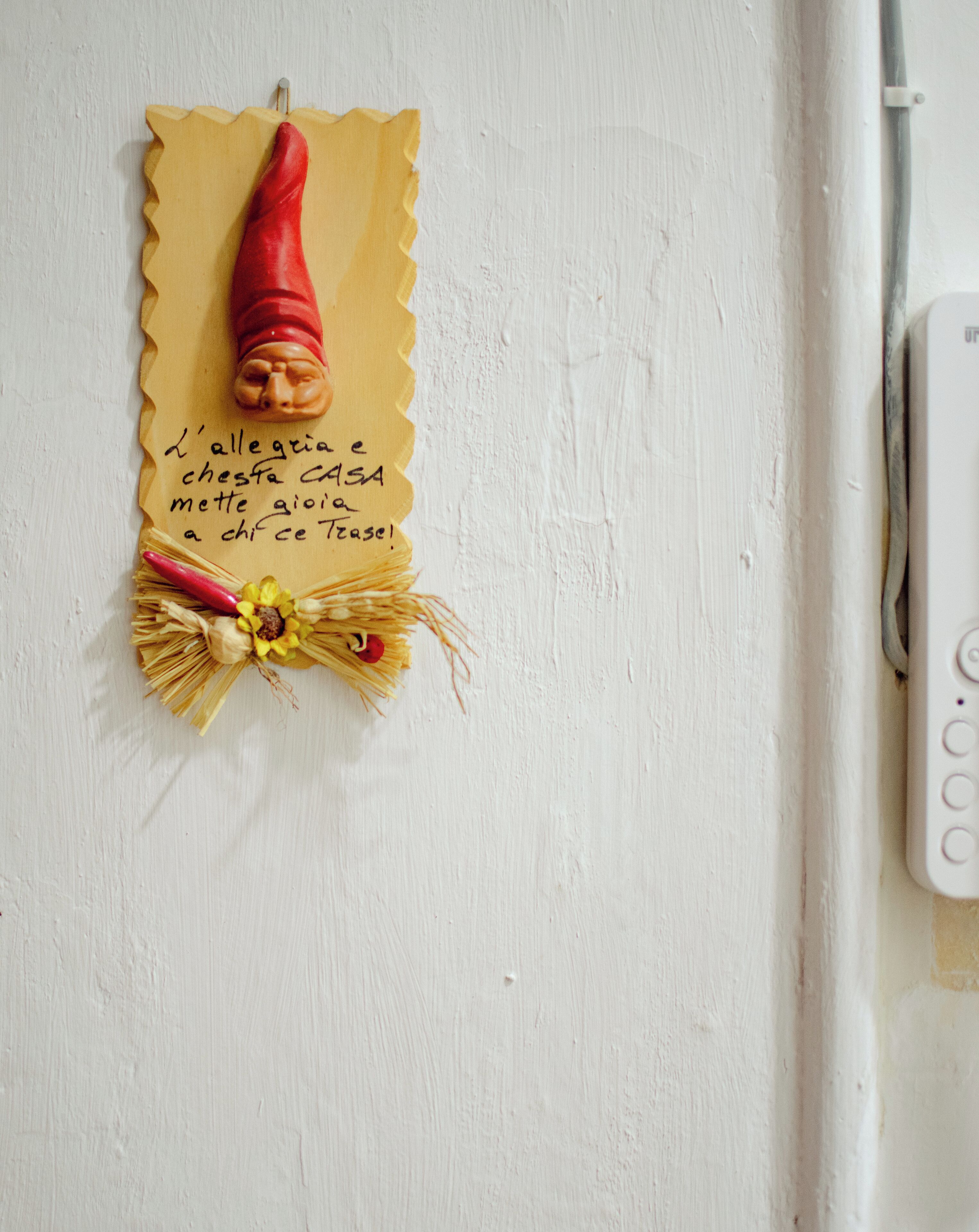 Een muur met een decoratieve wandhanger, een handgeschreven briefje en een klein bloemstuk.