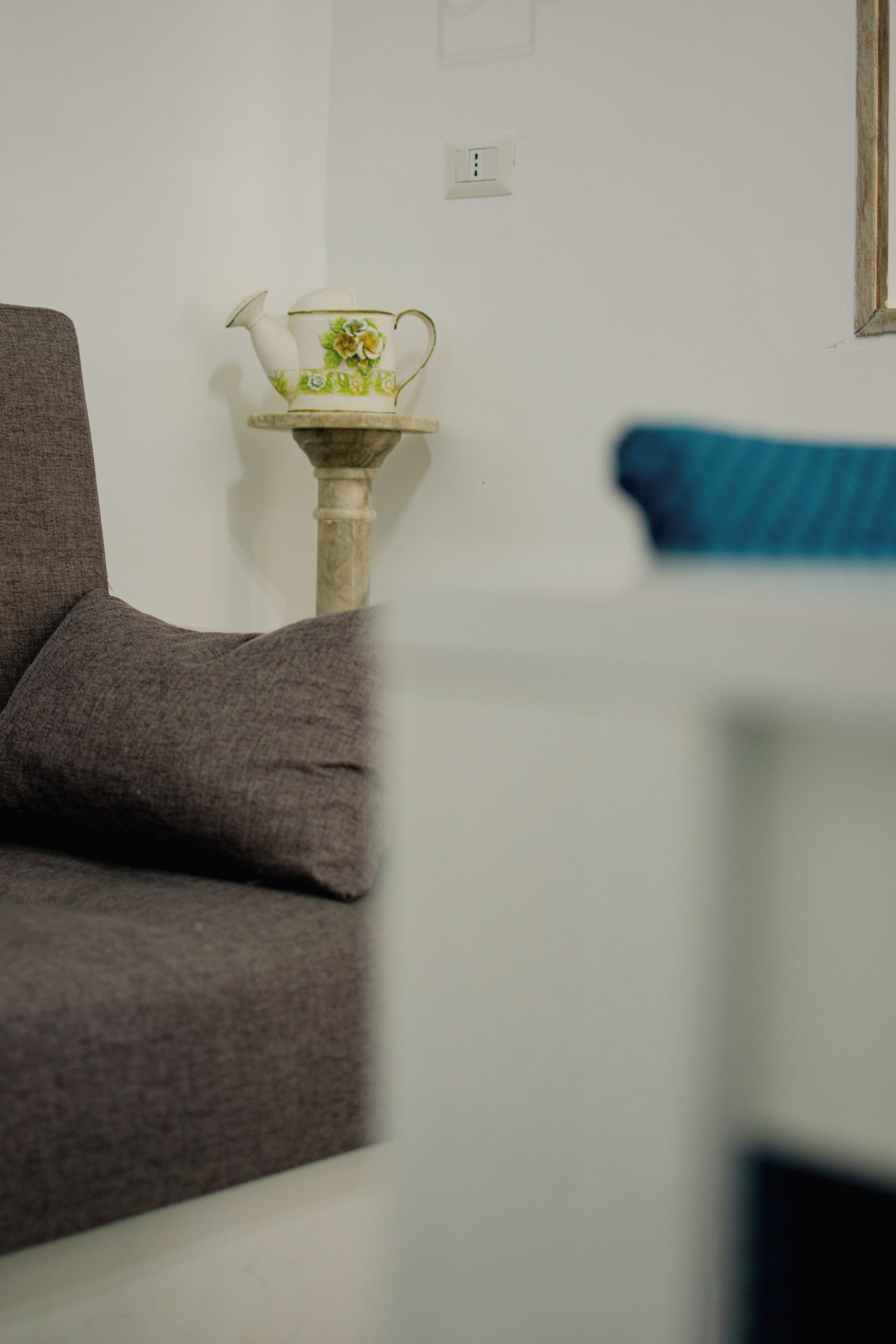 Een kamer met een grijze bank, een witte tafel met een decoratief object, en een blauw kussen.