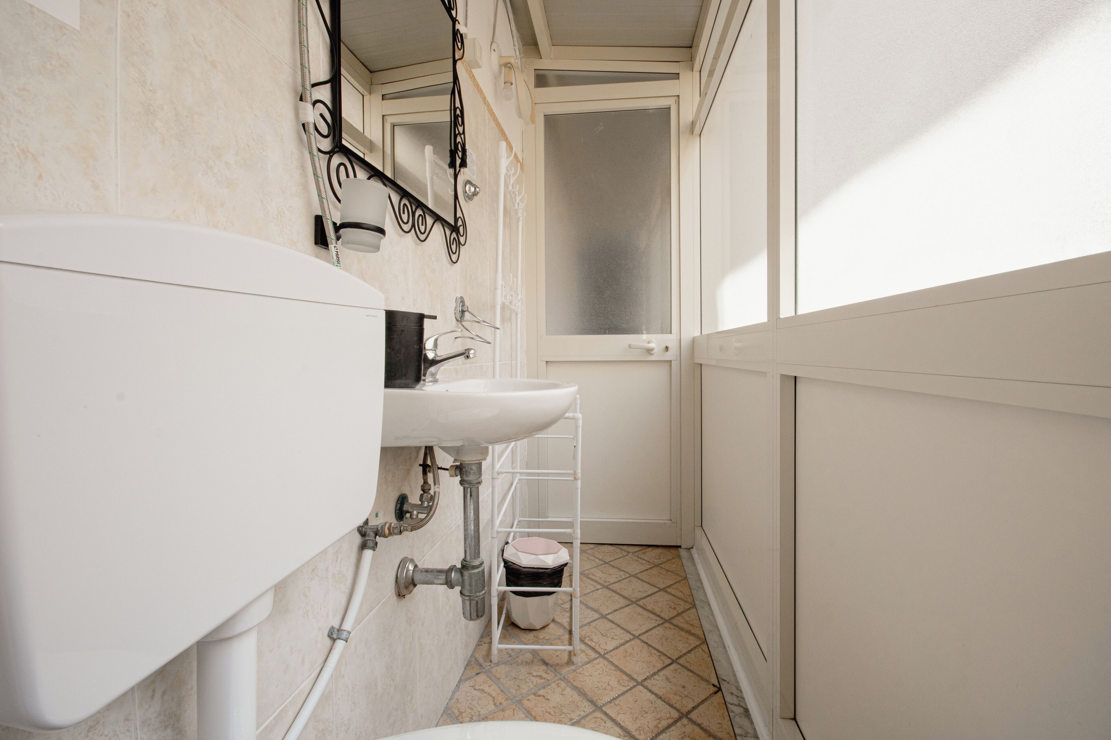 A bathroom with a toilet, sink, and a small shelf with a trash bin.
