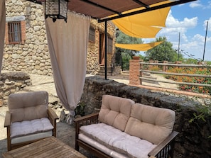 Un área de estar al aire libre con dos sillones acolchados y un sofá, una pared de piedra, una columna de ladrillo y un dosel amarillo.