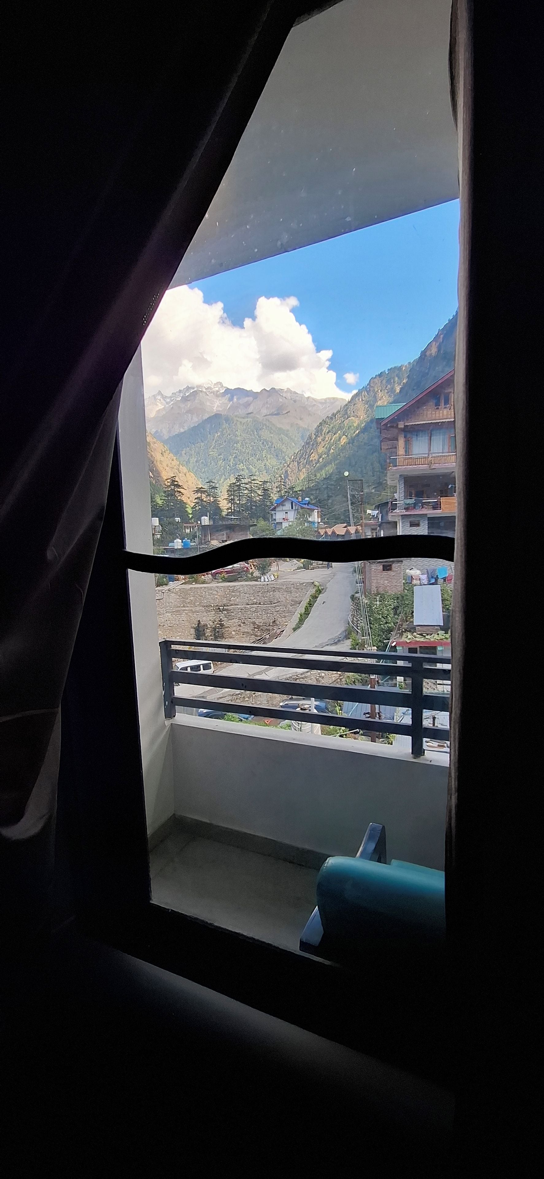 Una habitación con vistas a un paisaje montañoso, un balcón con barandilla y una ventana con cortinas.