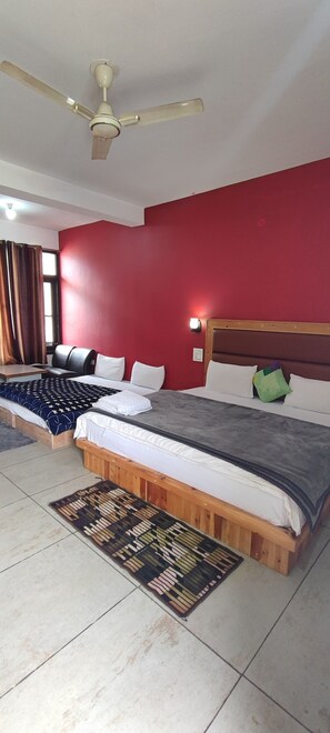 A bedroom with two beds, a ceiling fan, a red wall, and a window with curtains. - Woodward 2 by 4wildflower (Bhuntar)