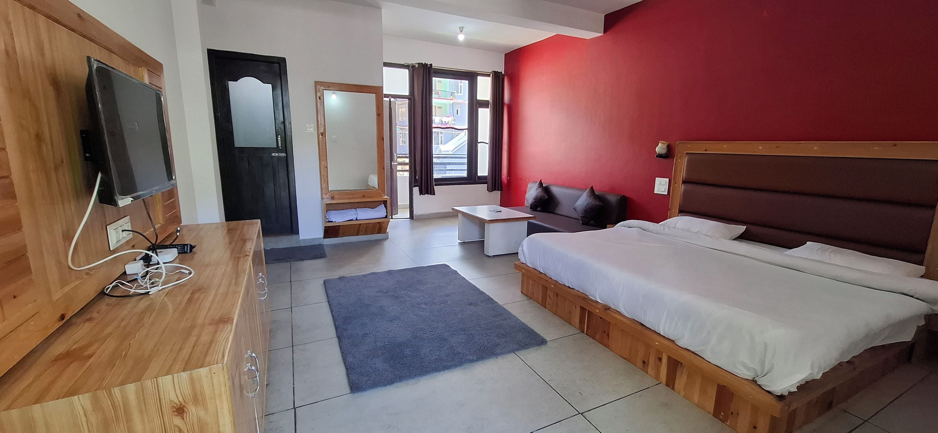 A hotel room with a bed, a desk, a television, and a view of a building outside.