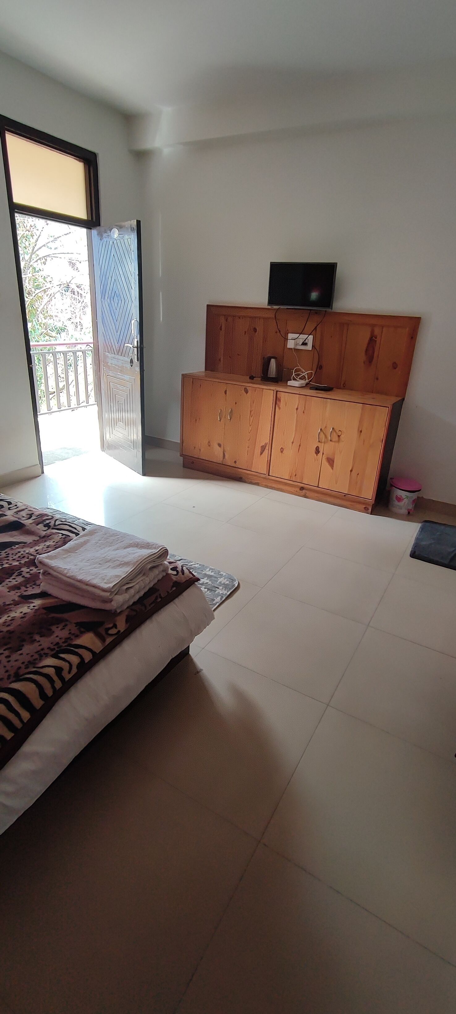 Un dormitorio con cama, un armario de madera, televisión y una puerta corrediza de vidrio que da a un balcón.
