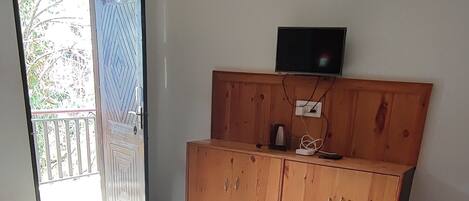 Un dormitorio con cama, un armario de madera, televisión y una puerta corrediza de vidrio que da a un balcón.