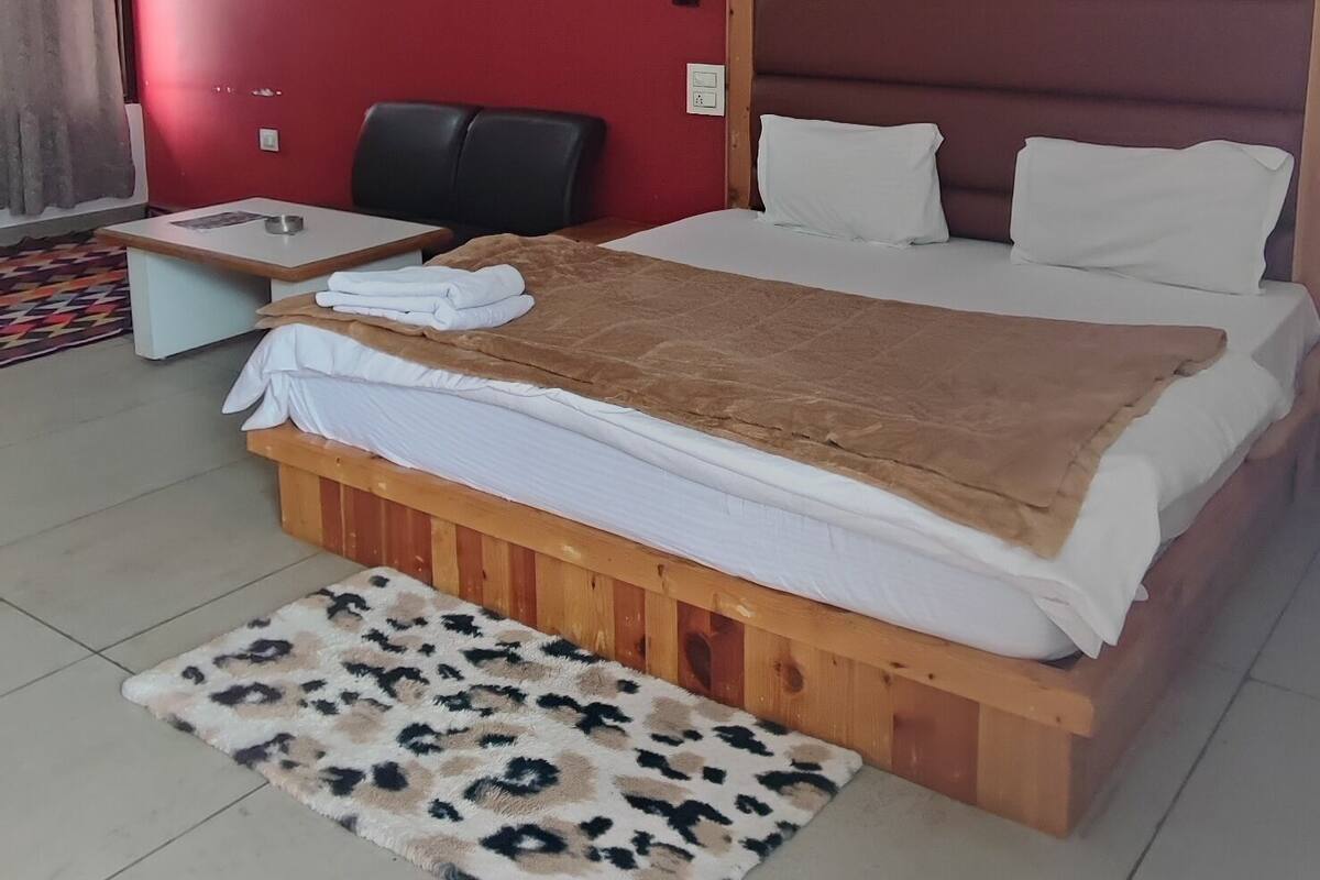 Un dormitorio con cama, ventilador de techo, pared roja y una mesita.