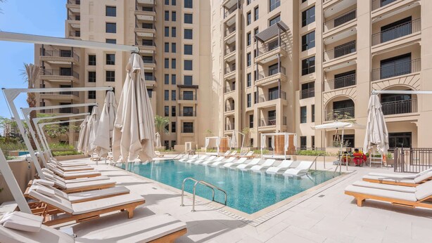 A poolside area with sun loungers and umbrellas, surrounded by a high-rise building with balconies. - G14 Jadeel 3 in Dubai (Dubai)