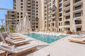 A poolside area with sun loungers and umbrellas, surrounded by a high-rise building with balconies. - G14 Jadeel 3 in Dubai (Dubai)