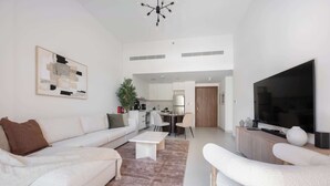 A modern living room with a sofa, a coffee table, and a TV. There is a kitchen area with cabinets and a dining table. - G14 Jadeel 3 in Dubai (Dubai)