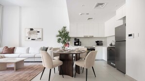 A modern kitchen with white cabinets, a stainless steel refrigerator, and a dining area with a round table and chairs. - G14 Jadeel 3 in Dubai (Dubai)