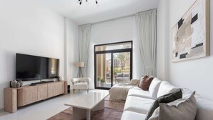 A modern living room with a flat-screen TV, a sofa, a coffee table, and a view through a large window. - G14 Jadeel 3 in Dubai (Dubai)