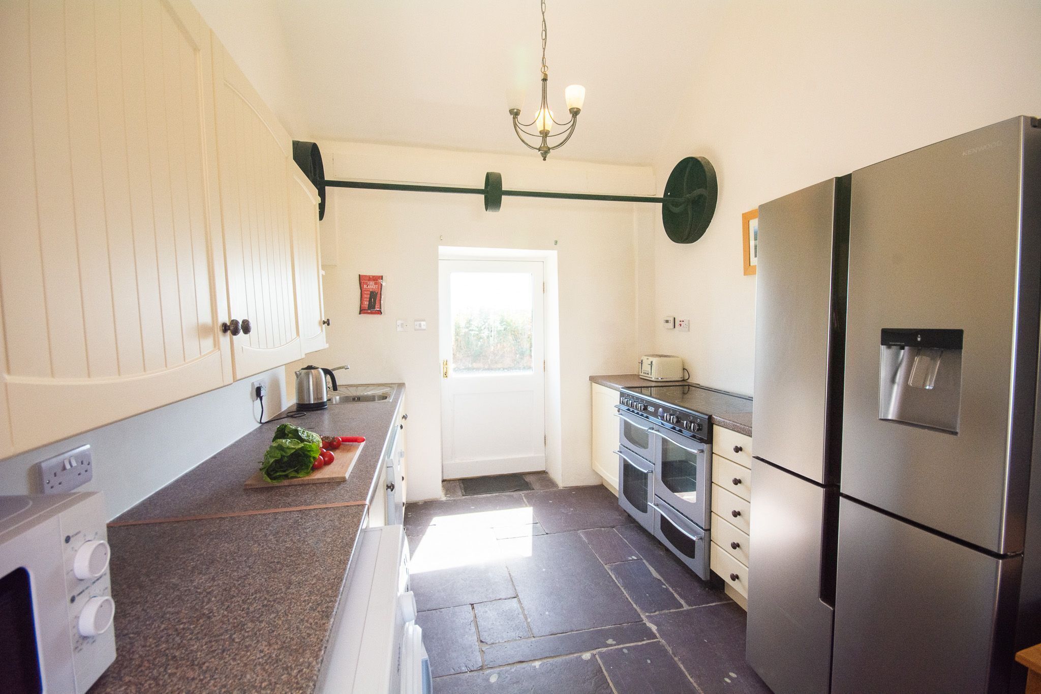 A kitchen with a stainless steel refrigerator, oven, and a wooden countertop with a cutting board and vegetables.