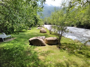 Un río con rocas y vegetación, un banco y vistas a montañas distantes.