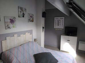 Un dormitorio con cama, televisor, armario y obras de arte en las paredes.