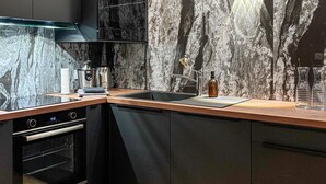 Una cocina moderna con un diseño elegante, que cuenta con un lavamanos de acero inoxidable, un horno empotrado y un salpicadero de mármol.