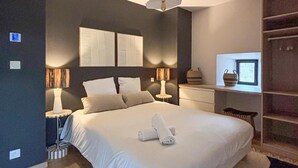 Un dormitorio moderno con una cama grande, dos mesitas de noche con lámparas, un cabecero con espejo y un ventanal con vistas.