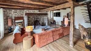 Una habitación rústica con pared de piedra, vigas de madera, un sofá, una lámpara y una chimenea.