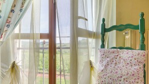 A room with a window, a green chair, and a floral pillow. - Room 'Agriturismo Cascina Favorita - D3' with Shared Garden and Wi-Fi (Castelletto Merli)