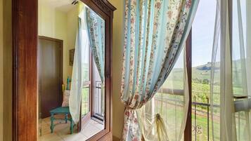 Ein Zimmer mit einem großen Spiegel, einem Fenster mit floralem Vorhang und Blick auf eine grüne Landschaft.