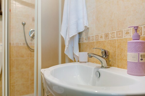 A bathroom with a white sink, a shower, and a towel hanging on the wall.