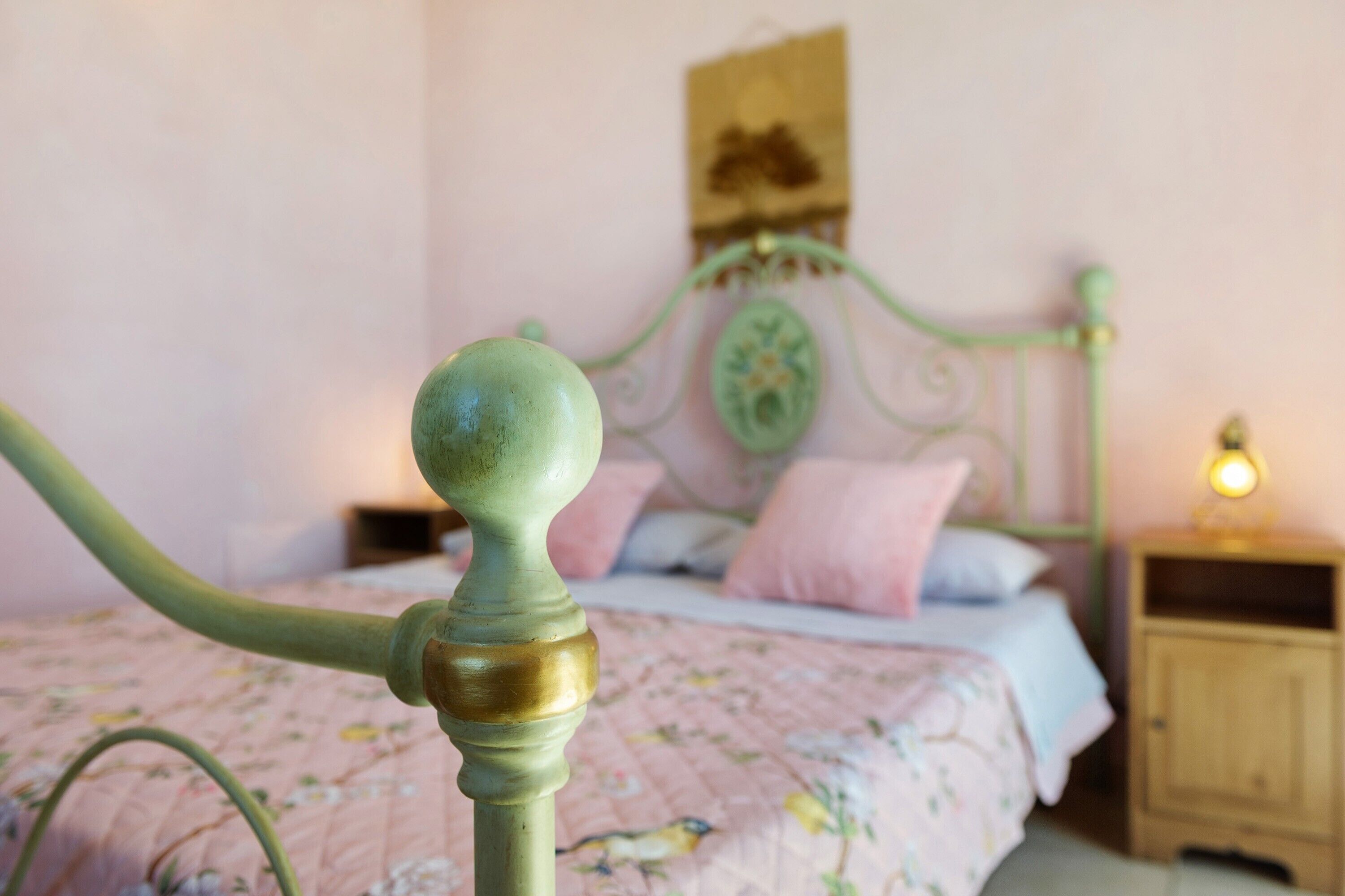 Un lit avec une couvre-lit à motifs floraux, une tête de lit en métal verte et une table de chevet avec une lampe.