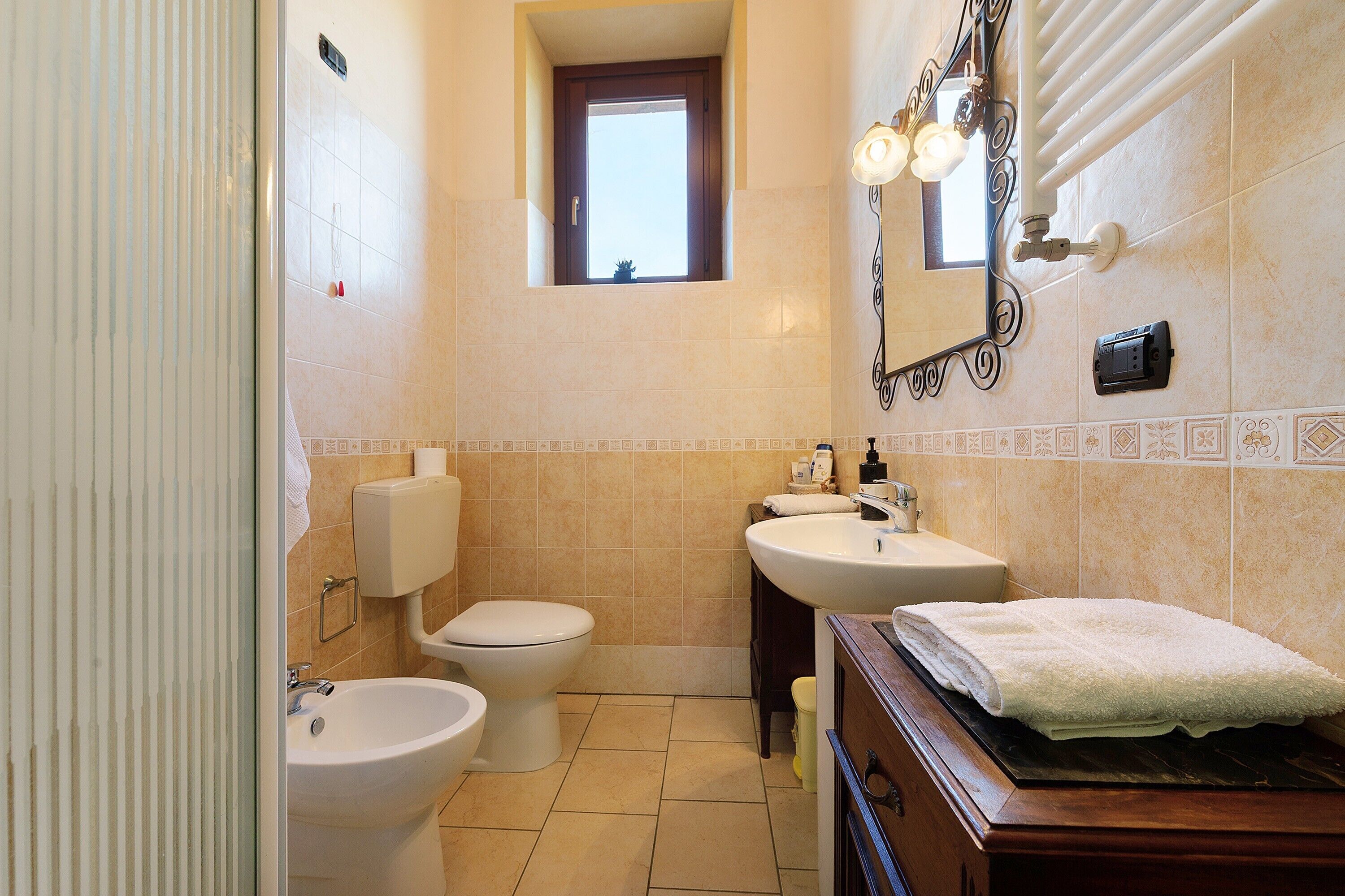 Ein Badezimmer mit Toilette, Bidet, Waschbecken und einem beleuchteten Spiegel.