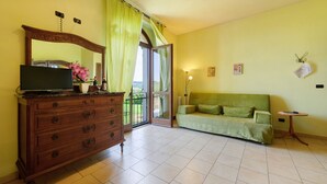 Una stanza con una cassettiera in legno, un divano verde, un tavolino, uno specchio e vista attraverso una porta vetrata.