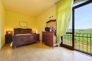 A bedroom with a bed, dresser, bedside lamps, and a window with a view of a green landscape.