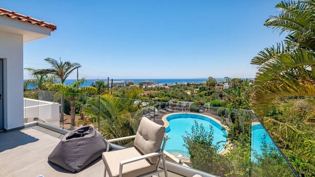 A rooftop pool with a clear view of the sea, surrounded by palm trees and lounge chairs. - Ayia Napa Panorama Villa (Ayia Napa)