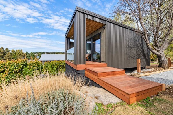 A modern house with a wooden deck, a large window, and a view of the surrounding landscape.