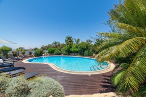 Une piscine à bords incurv és, dotée de chaises longues et agrémentée d’un aménagement paysager de style tropical.